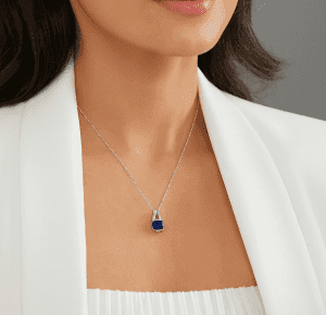 قلادة راقية من الألماس أو الحجر الكريم تتدلّى على عنق امرأة أنيقة ترتدي الأبيض؛ Elegant diamond or gemstone pendant necklace showcased on the neck of a stylish woman in white; Элегантная подвеска из бриллианта или драгоценного камня на шее женщины в белом наряде.