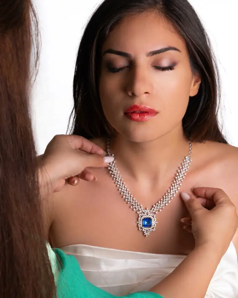 Home 1 11 Custom-made gold and diamond necklace with blue gemstone being fitted on a model – handcrafted jewelry in Dubai.