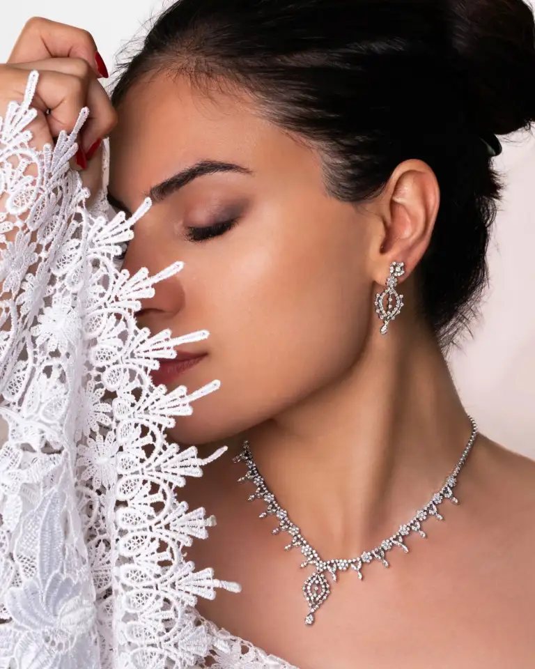 Home 1 12 Close-up of a bride wearing a fine Jewellery set made of white gold and natural Diamonds, featuring an elegant necklace and matching earrings beside delicate lace.